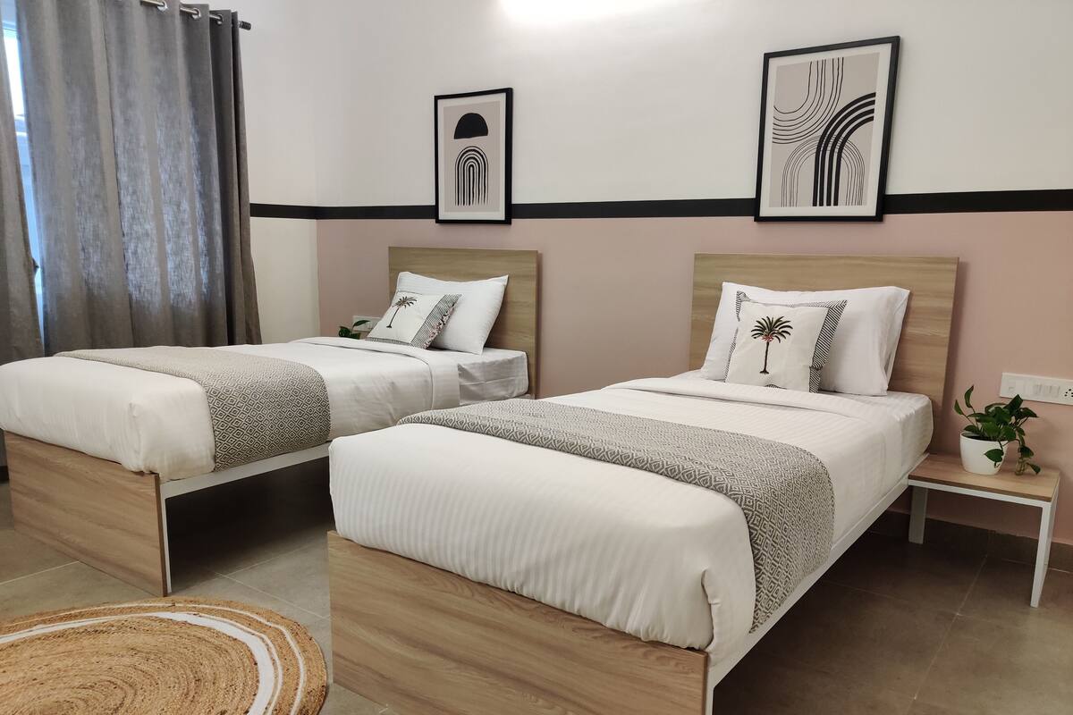 A hotel room with two beds, a small bedside table with a plant, and artwork on the walls.