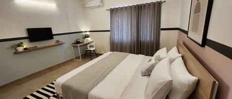 A neatly arranged bedroom with a bed, bedside table, chair, and a desk with a chair.