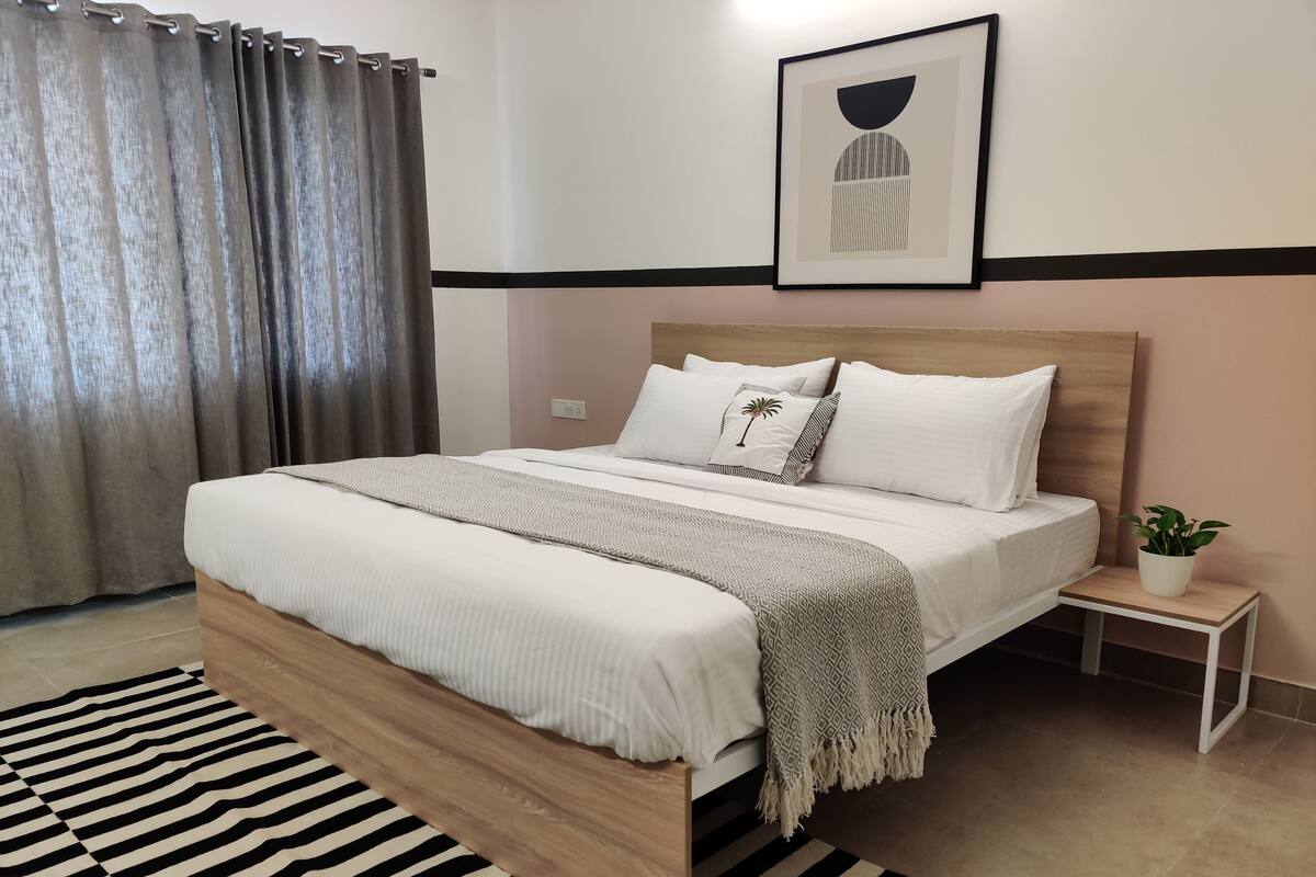A neatly made bed with a wooden frame, a bedside table with a plant, and a striped rug.