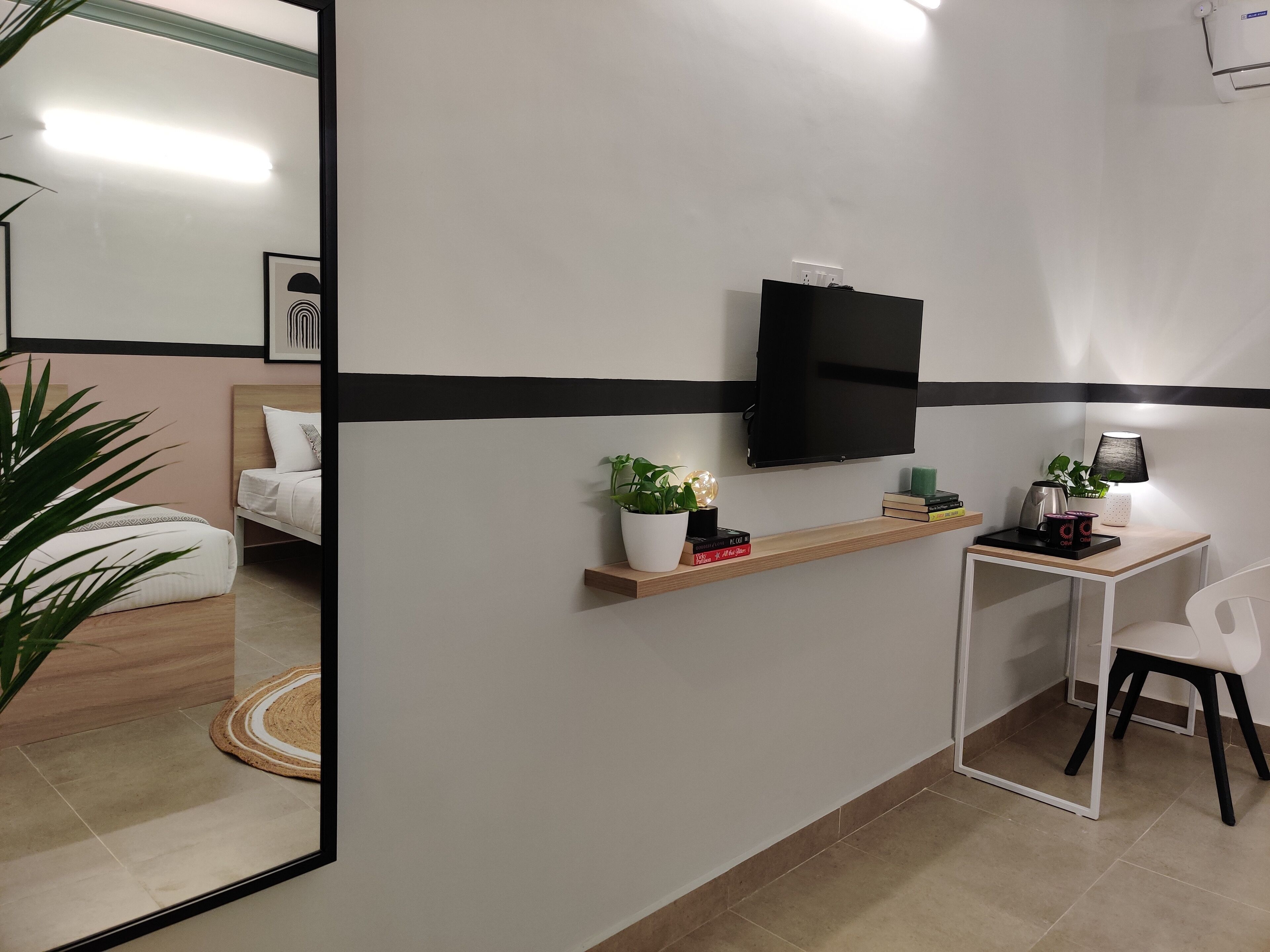 A modern hotel room with a bed, a desk, a chair, a TV, and a shelf with decorative items.