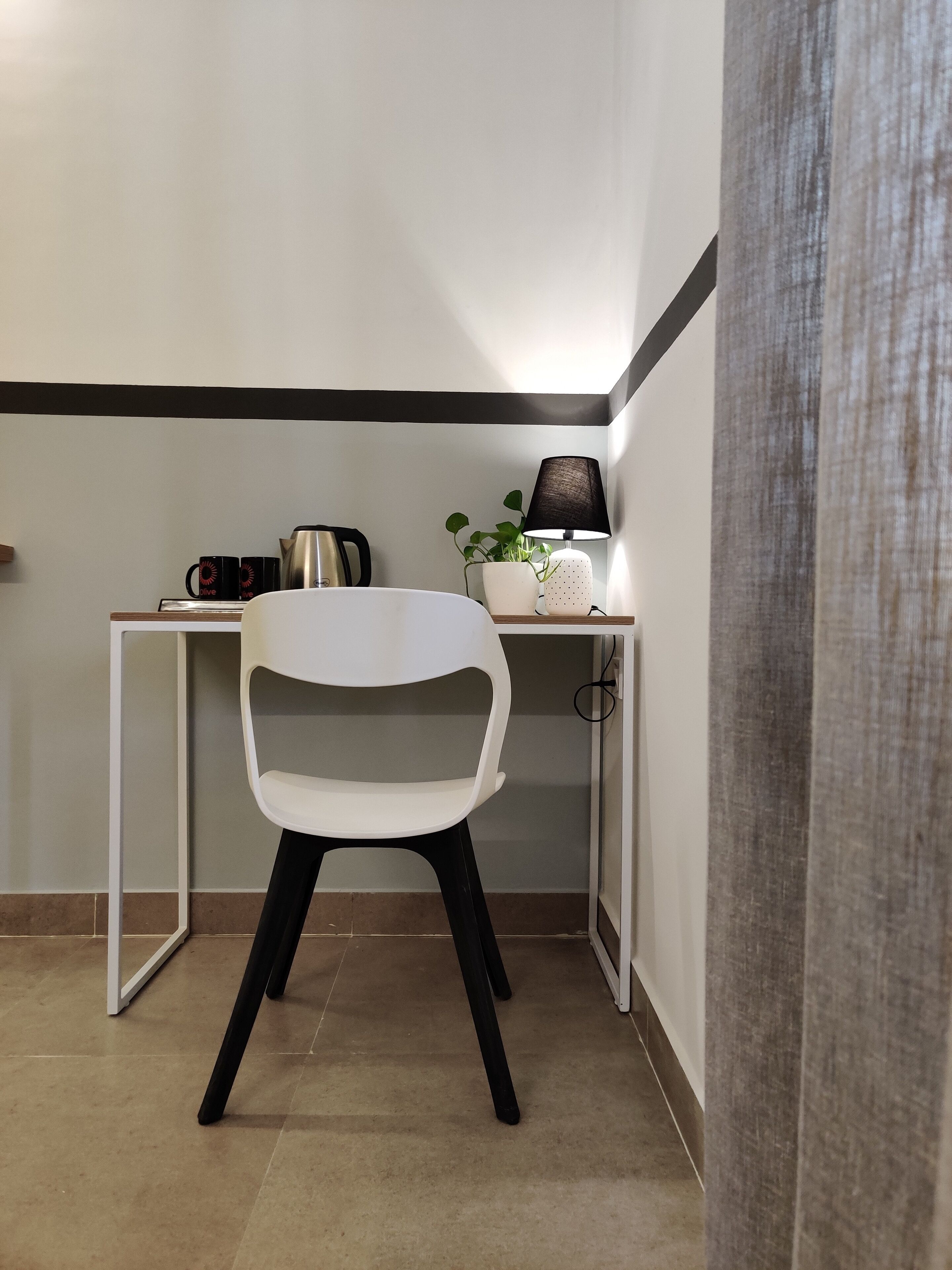 A small, modern kitchenette with a white chair, a coffee maker, and a plant on the counter.