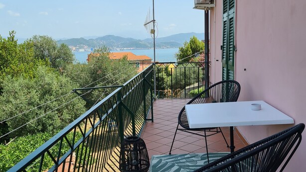 Un balcon avec une table et des chaises, offrant une vue panoramique sur une étendue d’eau et des collines lointaines.