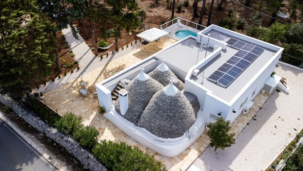 Een modern huis met een zwembad, zonnepanelen en een bijzondere koepelstructuur van steen.
