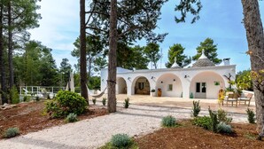 Een witte villa met meerdere bogen, omgeven door bomen en een grindpad.
