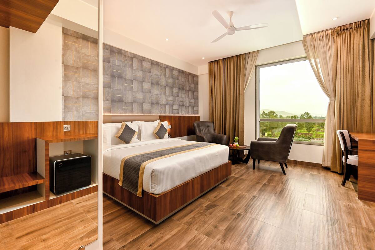 A modern hotel room with a large bed, a desk, and a view of the outdoors.