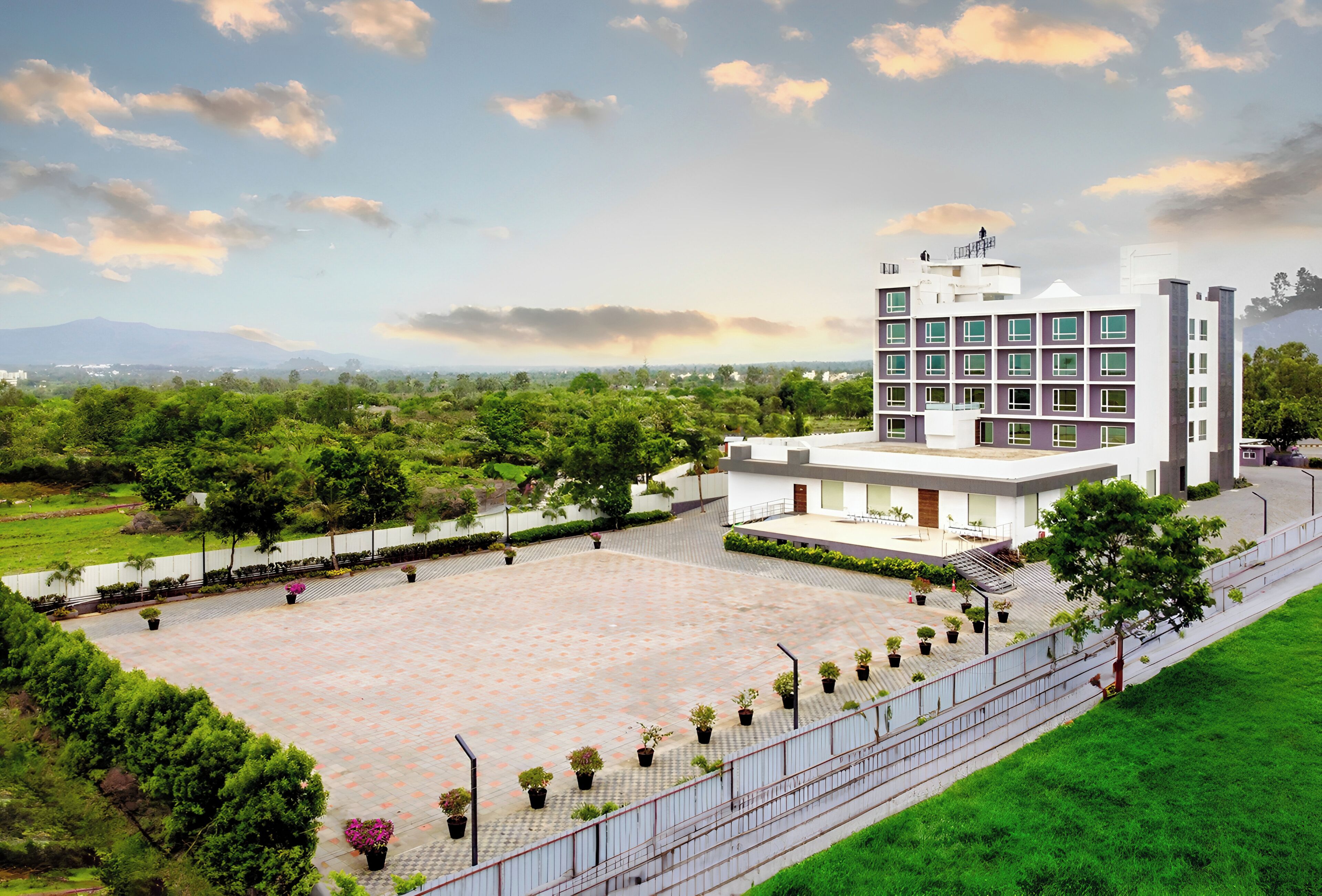 A modern building with a spacious courtyard, surrounded by greenery and a clear sky.