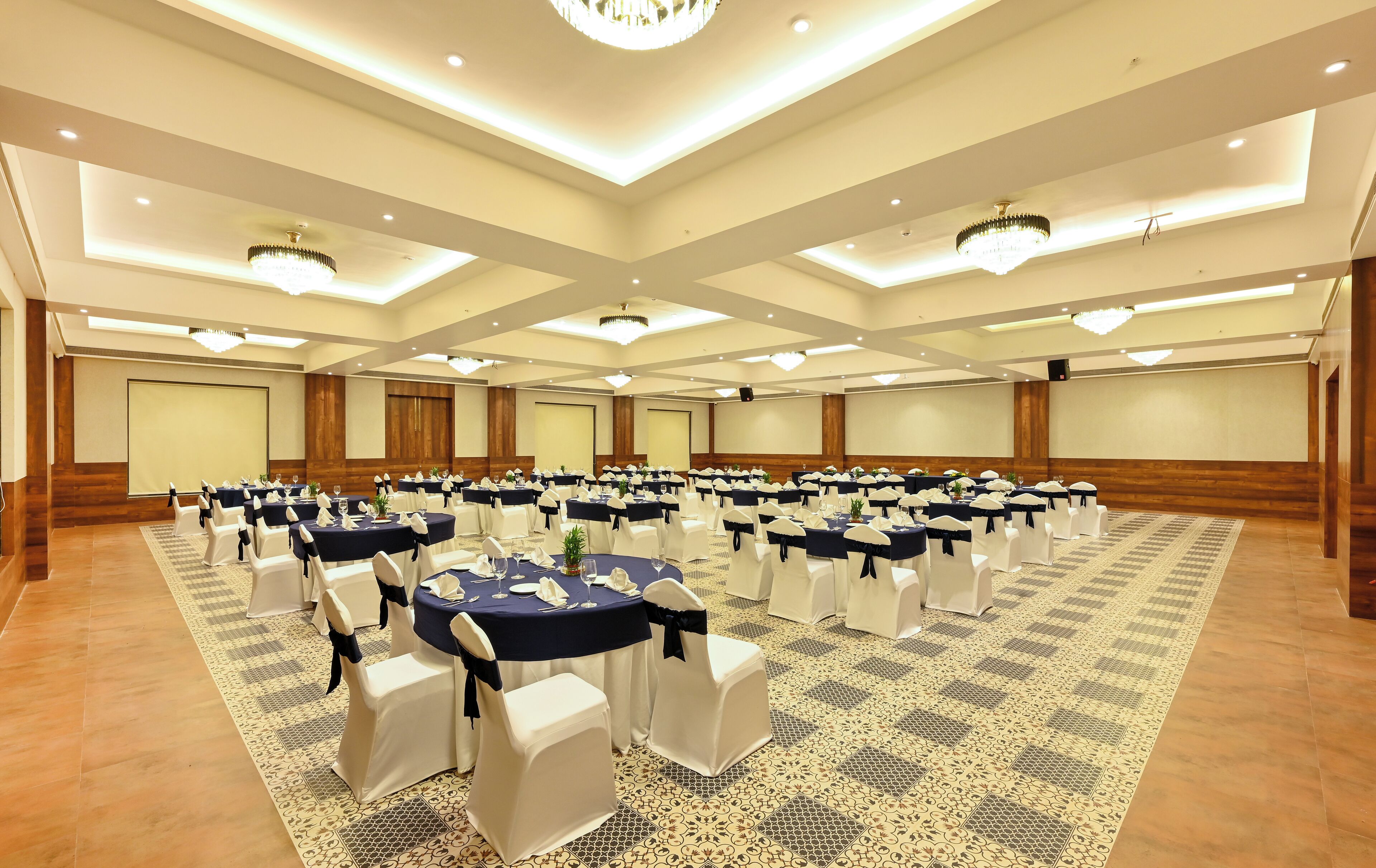 A large conference room with multiple round tables, white chairs with navy sashes, and a patterned carpet.