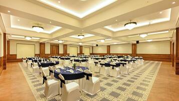 A large conference room with multiple round tables, white chairs with navy sashes, and a patterned carpet.