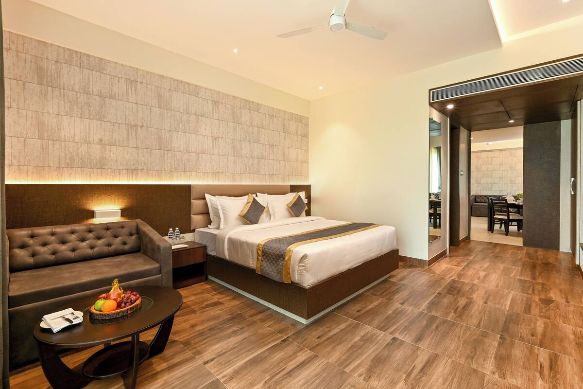 A modern hotel room with a large bed, a sofa, a small table with fruit, and a ceiling fan.