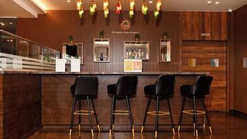 Uma área de bar moderna com estilo retrô, painéis de madeira, um balcão e três banquetas pretas.