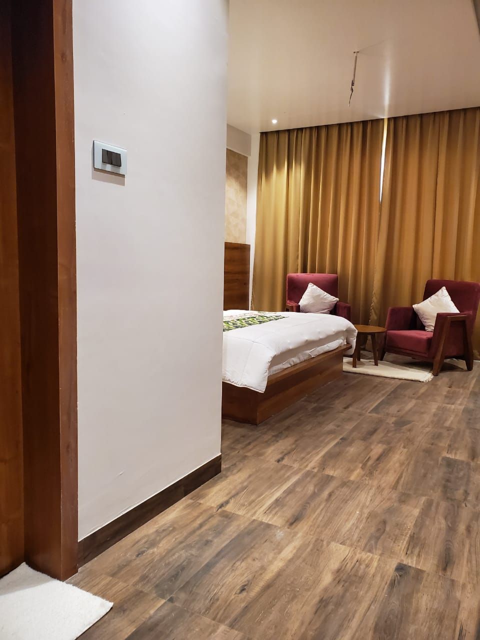 A hotel room with a bed, two chairs, a small table, and a curtain.