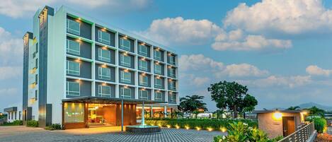 A modern hotel with a spacious entrance, a well-maintained garden, and a clear view of the sky.