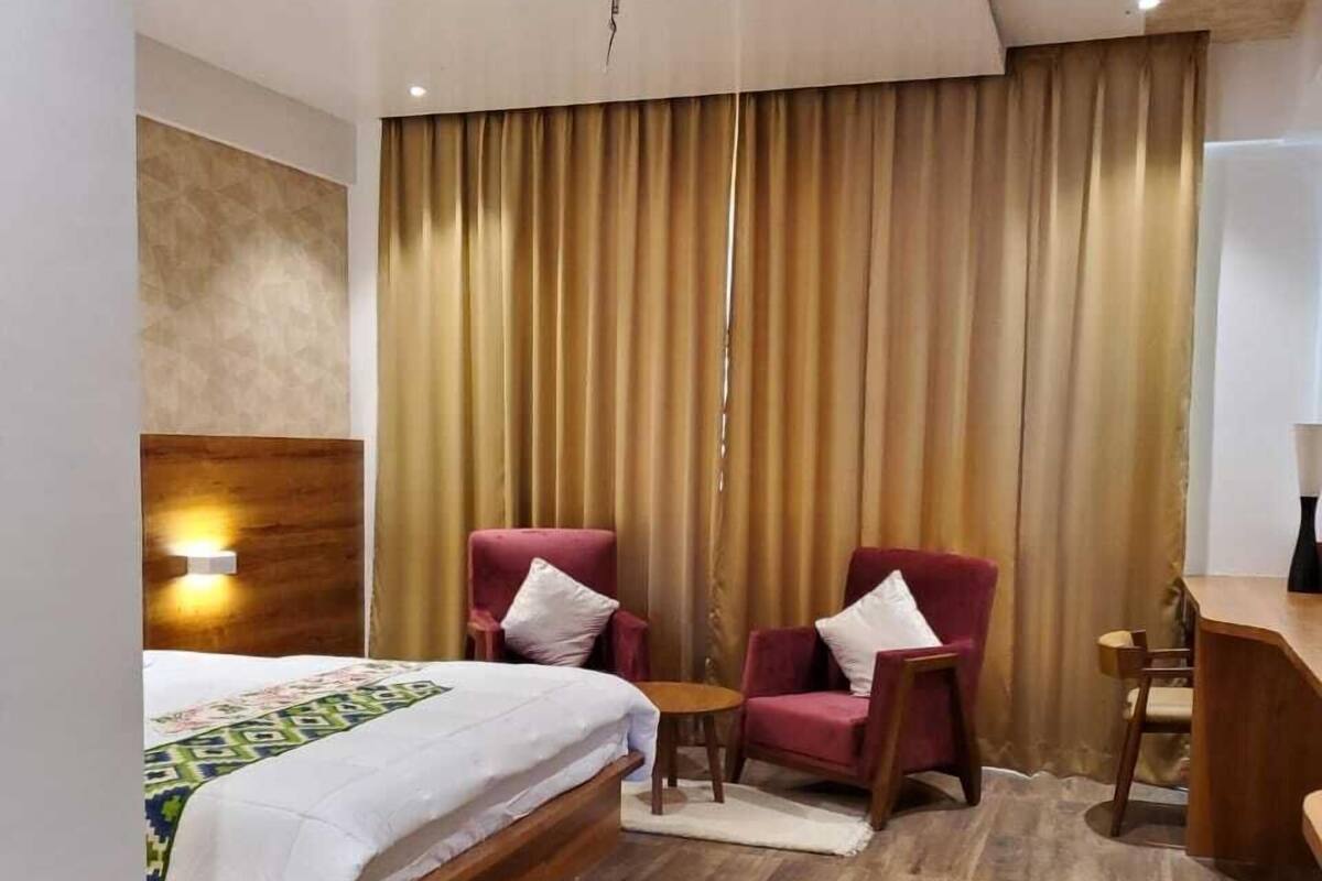 A hotel room with a bed, two red armchairs, a small table, and a desk.
