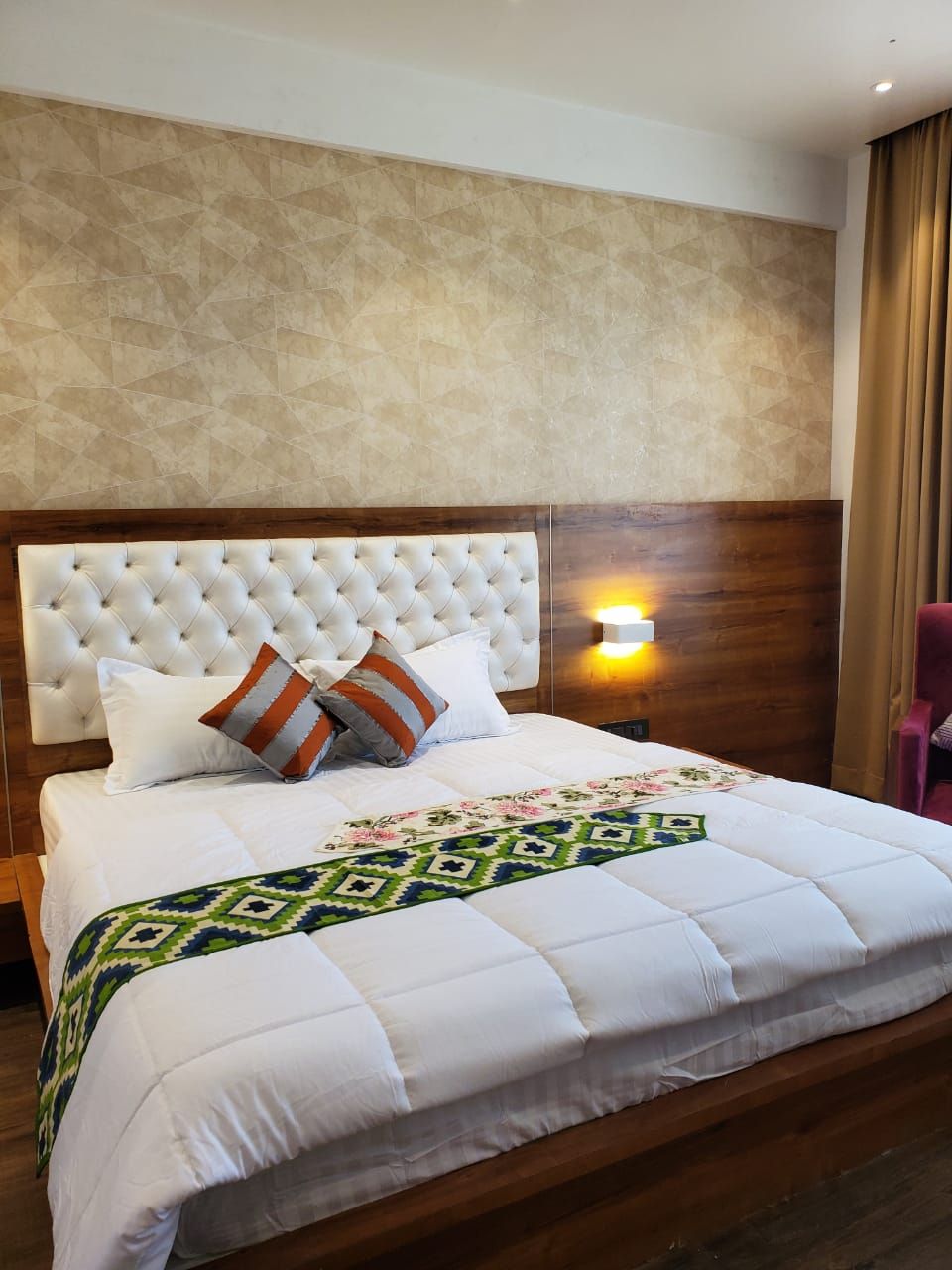 A hotel room with a large bed, a wooden headboard, a wall-mounted light, and a curtain.