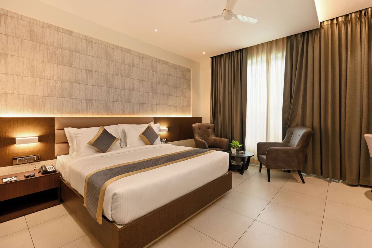 A modern hotel room with a large bed, a desk, a chair, and a ceiling fan.