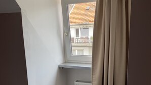 Een klein, afgesloten balkon met een raam, een radiator en beige gordijnen.