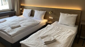 Hotelkamer met twee bedden, elk voorzien van witte lakens en kussens, een nachtkastje met een lamp, en een raam met gordijnen.