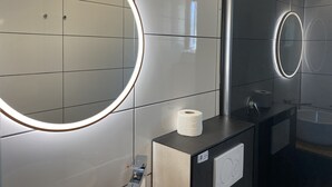 Een moderne badkamer met een grote spiegel, een toiletpapierautomaat en een wastafel.