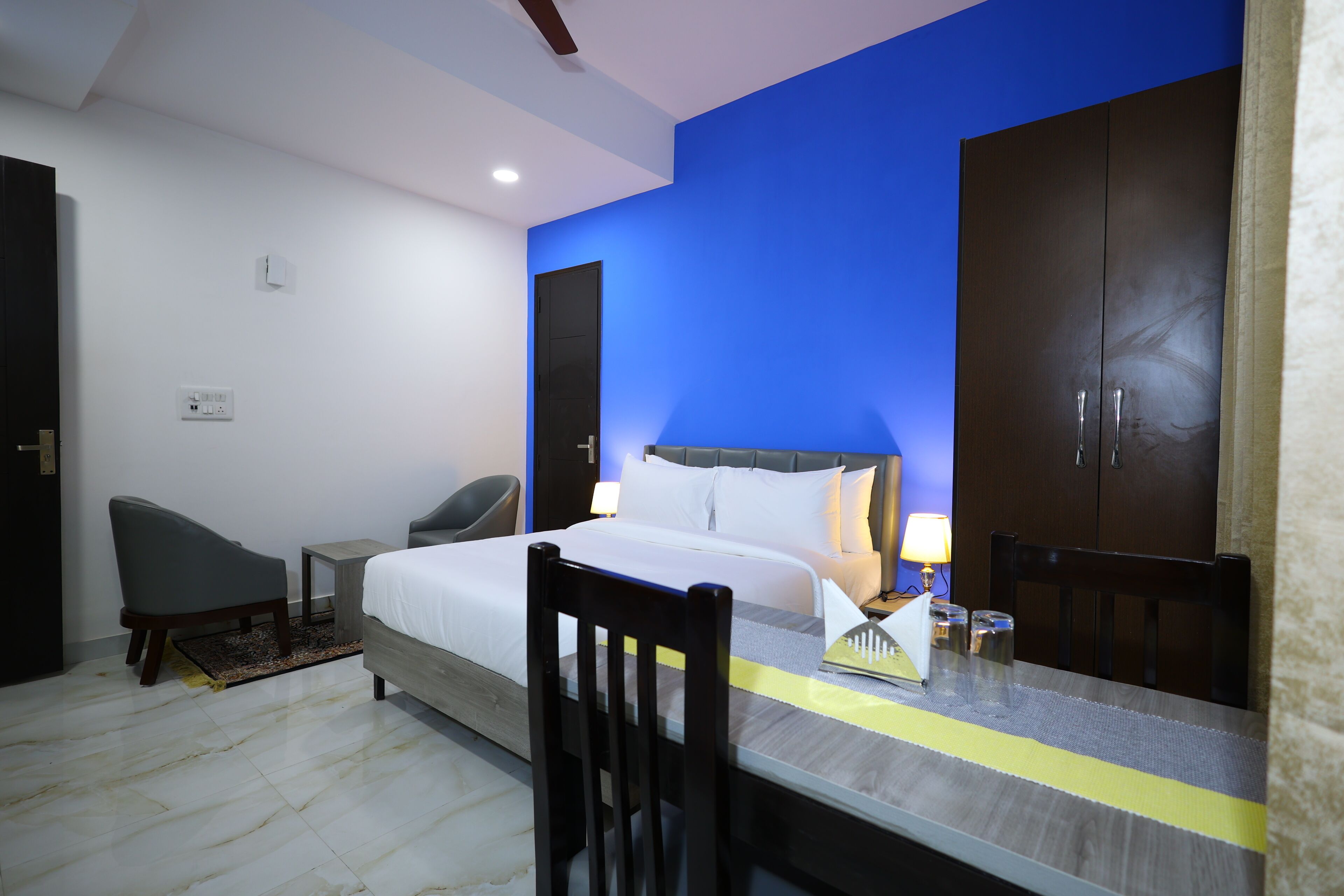 A hotel room with a bed, a desk, a chair, a wardrobe, and a nightstand.