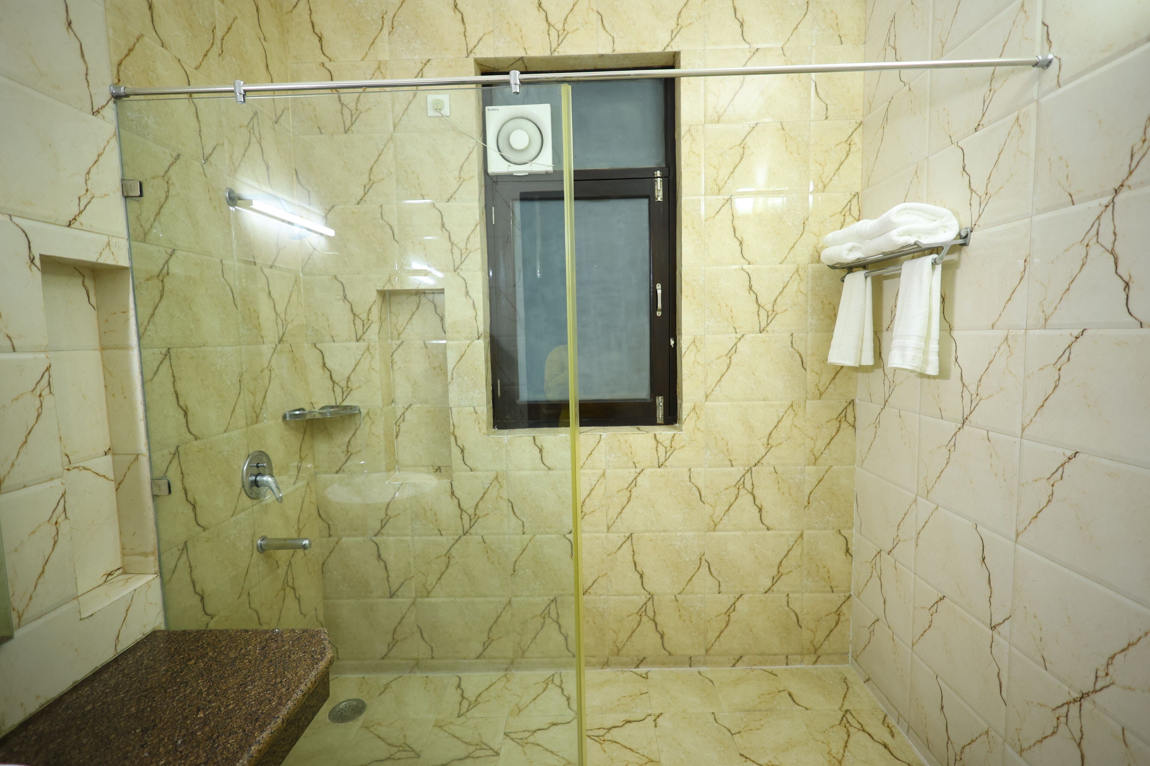 A bathroom with a glass-enclosed shower, a towel rack, and a small window.