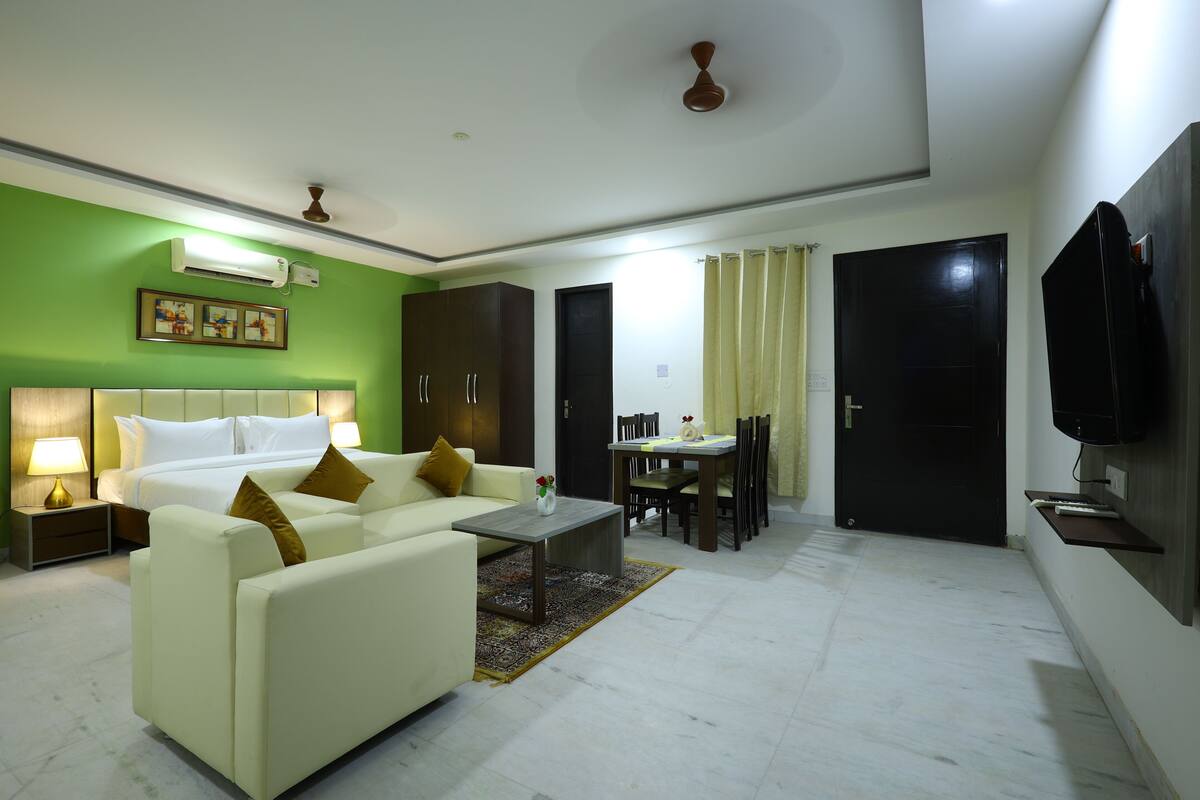 A modern living room with a sofa, a coffee table, a dining table with chairs, a TV mounted on the wall, and a ceiling fan.