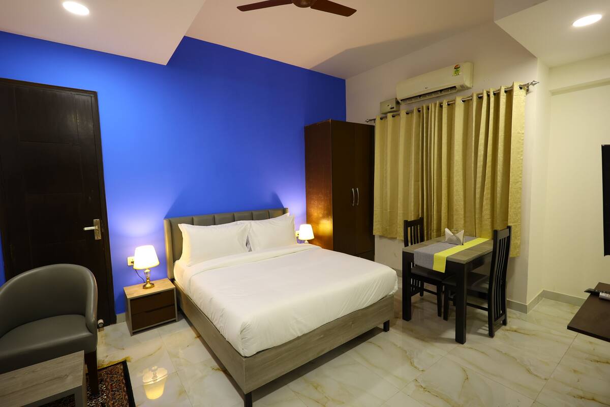A hotel room with a bed, bedside table, lamp, chair, desk, and curtains.