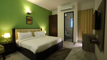 A hotel room with a bed, bedside lamps, a television, a wardrobe, and a bathroom visible through an open door.