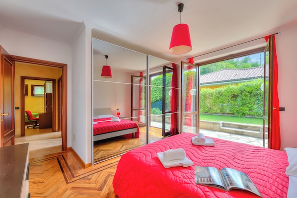 Habitación de hotel con una cama grande, escritorio, silla y vistas a la vegetación por la puerta de cristal.