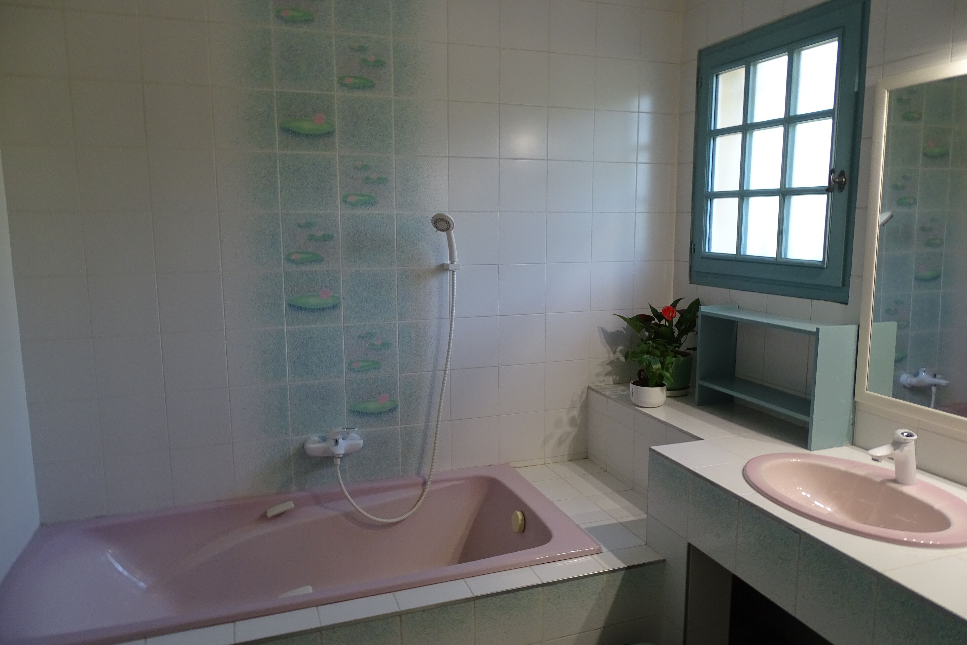 A bathroom with a pink bathtub, a sink, a window, and a mirror.