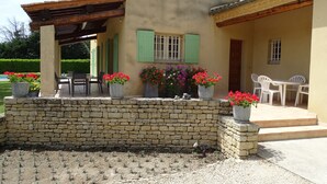 A stone wall with potted flowers, a covered patio, and a building with green shutters and a tiled roof. - Villa "La Verdoulento" au Calme et à L'abri des Regards Avec Piscine 6mx12m (AVIGNON)