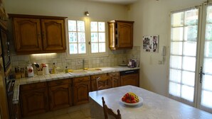 A kitchen with wooden cabinets, a marble countertop, a sink, and a window with curtains. - Villa "La Verdoulento" au Calme et à L'abri des Regards Avec Piscine 6mx12m (AVIGNON)