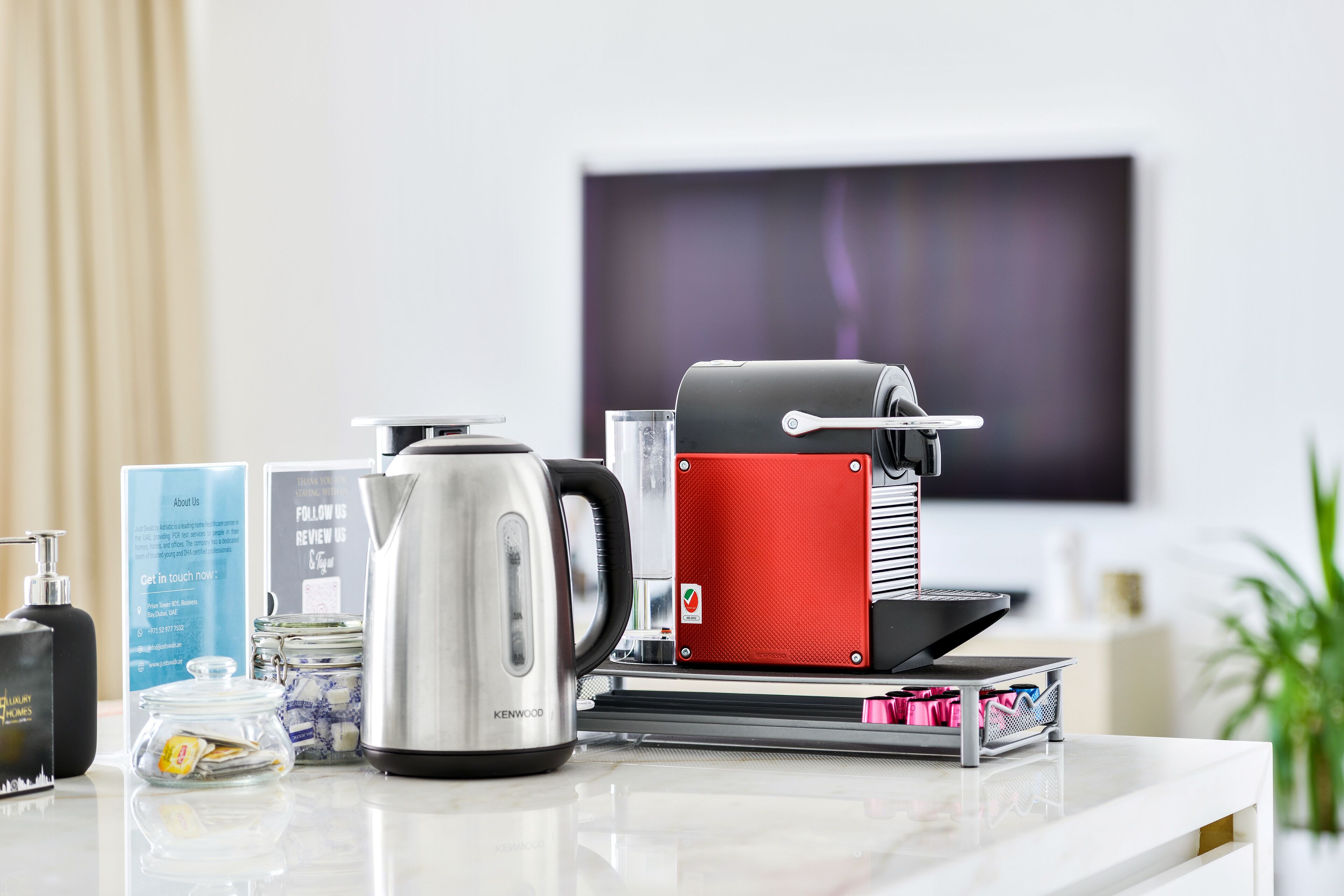 A modern kitchen with a coffee maker, kettle, and a red appliance on a countertop.