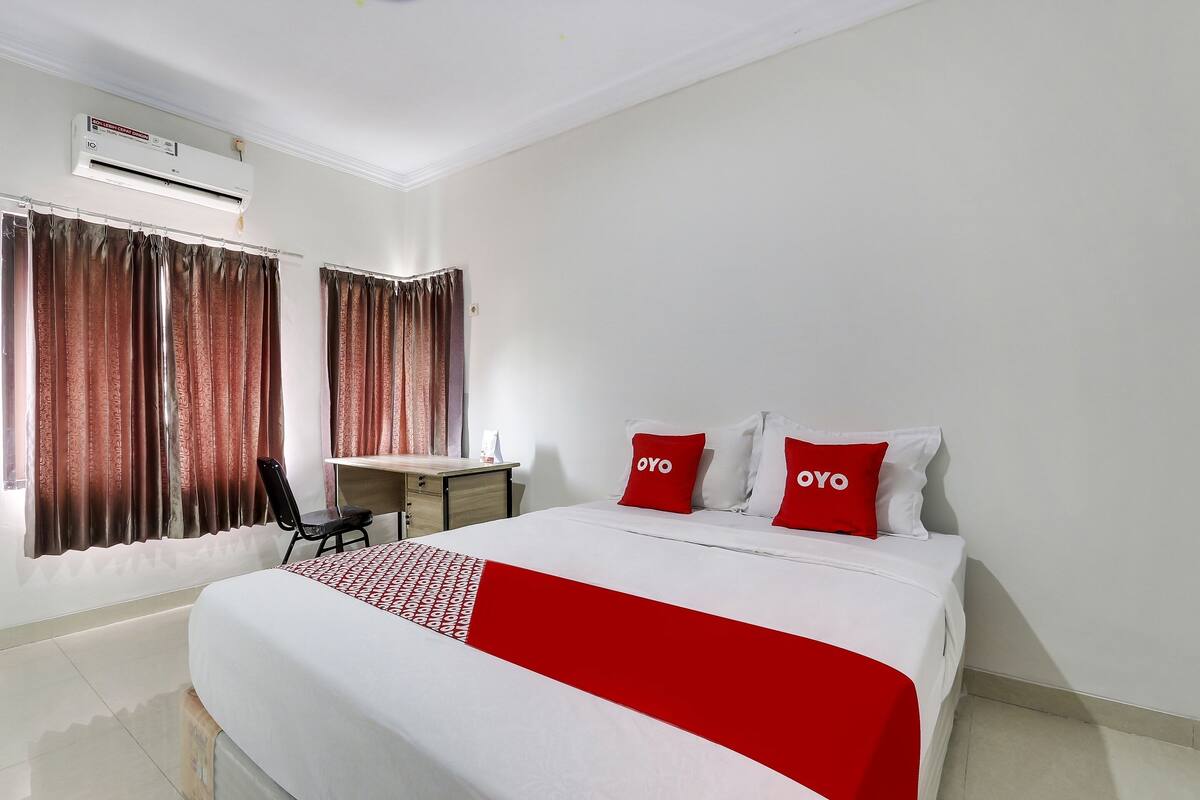 A hotel room with a bed, two pillows with "OYO" branding, a desk, and an air conditioning unit.