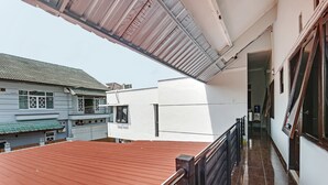 Un edificio residencial con techo rojo, un balcón con barandilla metálica y una pared exterior blanca.