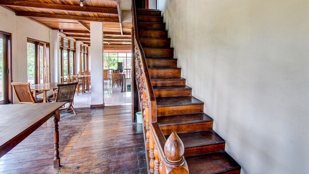 Un escalier en bois, doté d’une rampe, mène à un espace repas aménagé avec des tables et des chaises.