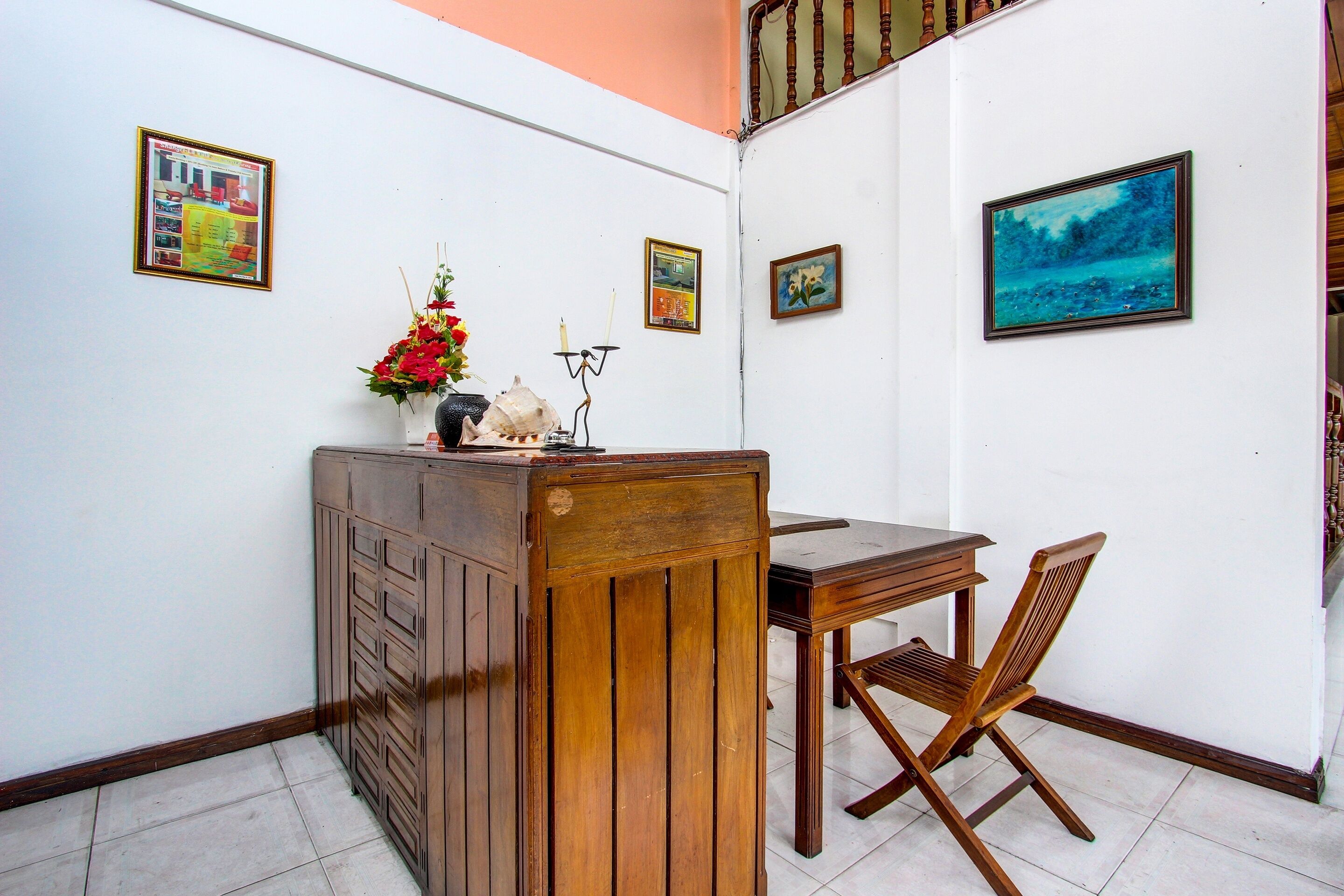 Quarto pequeno com escrivaninha de madeira, uma cadeira e um armário. Há três quadros nas paredes.