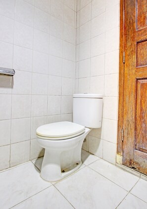 Et badeværelse med et hvidt toilet, flisegulv og en trædør.