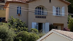 A two-story building with a tiled roof, a small balcony, and a window with shutters.