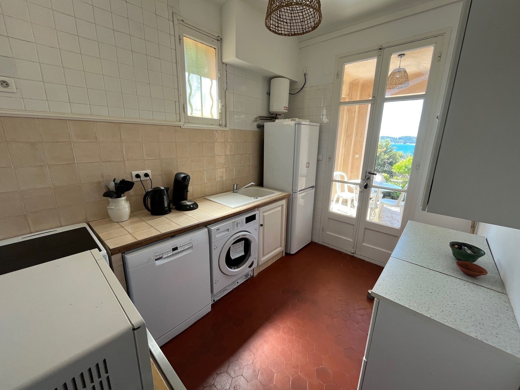 Een kleine keuken met een wasmachine, een koffiezetapparaat en een koelkast.