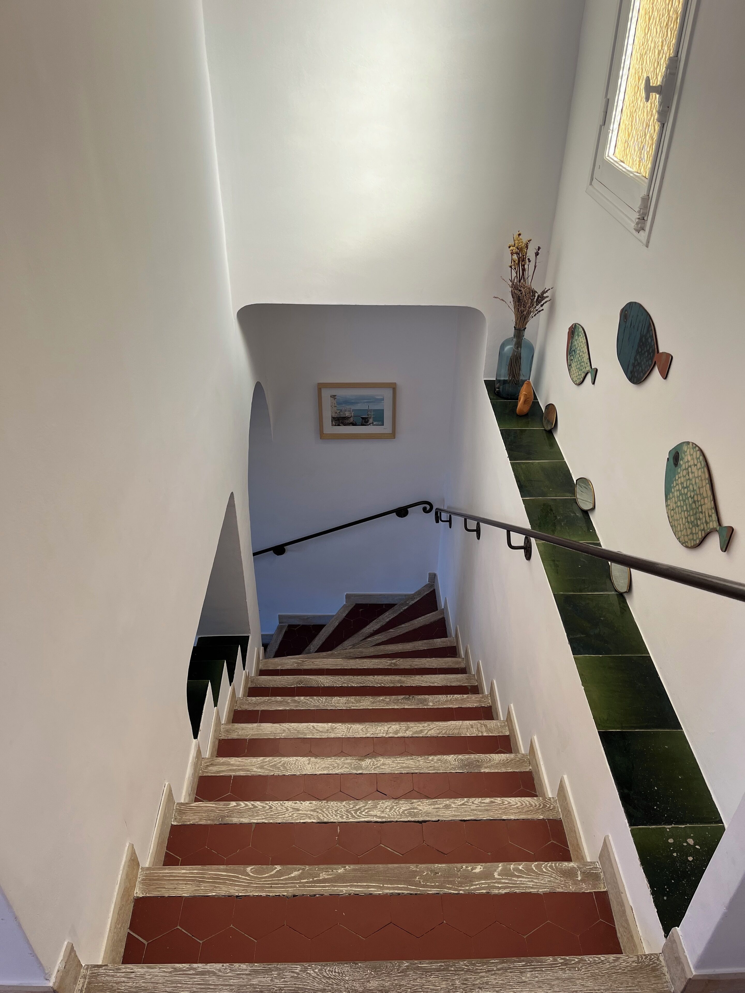 A staircase with wooden steps and a metal handrail, leading to a landing with a framed picture and decorative fish wall art.