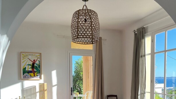 A dining area with a round table, chairs, a hanging light fixture, and a view of the outdoors.