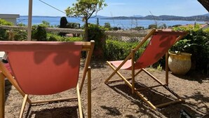Two red folding chairs with a view of the sea and hills in the background.