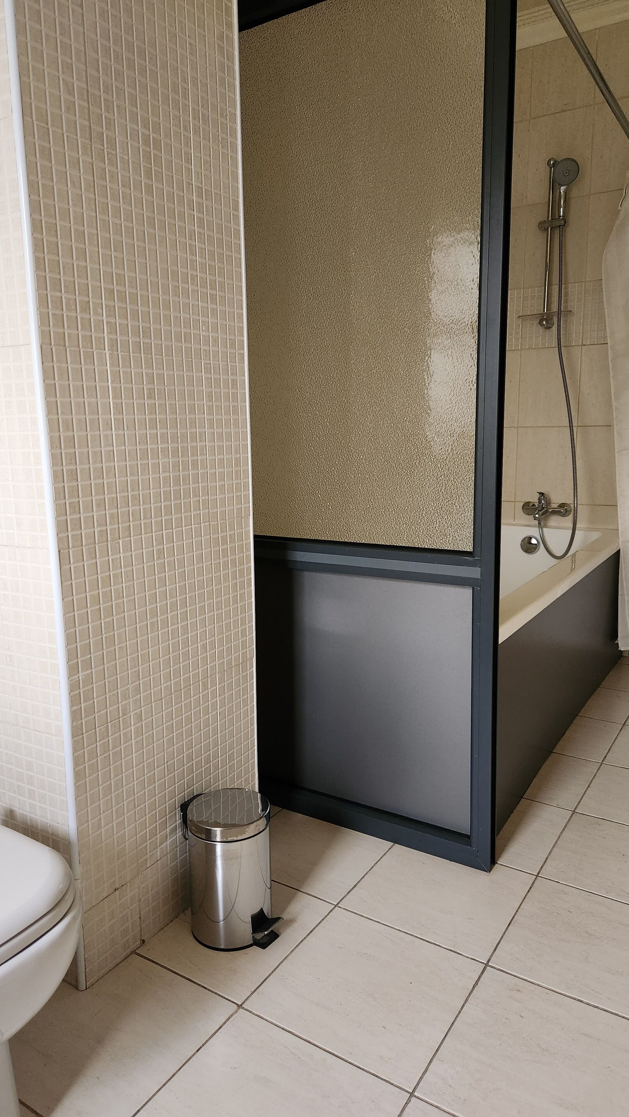 A bathroom with a toilet, a trash bin, a shower, and a bathtub.