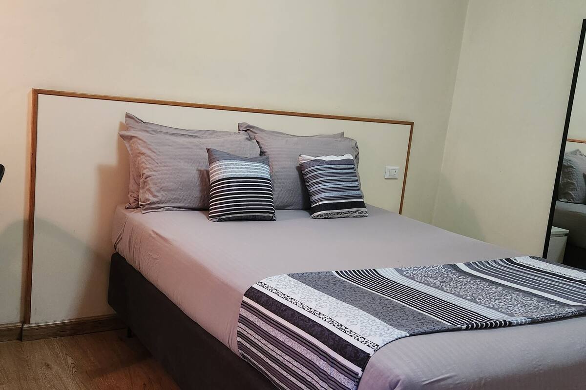 A bedroom with a bed, a desk, and a mirror.