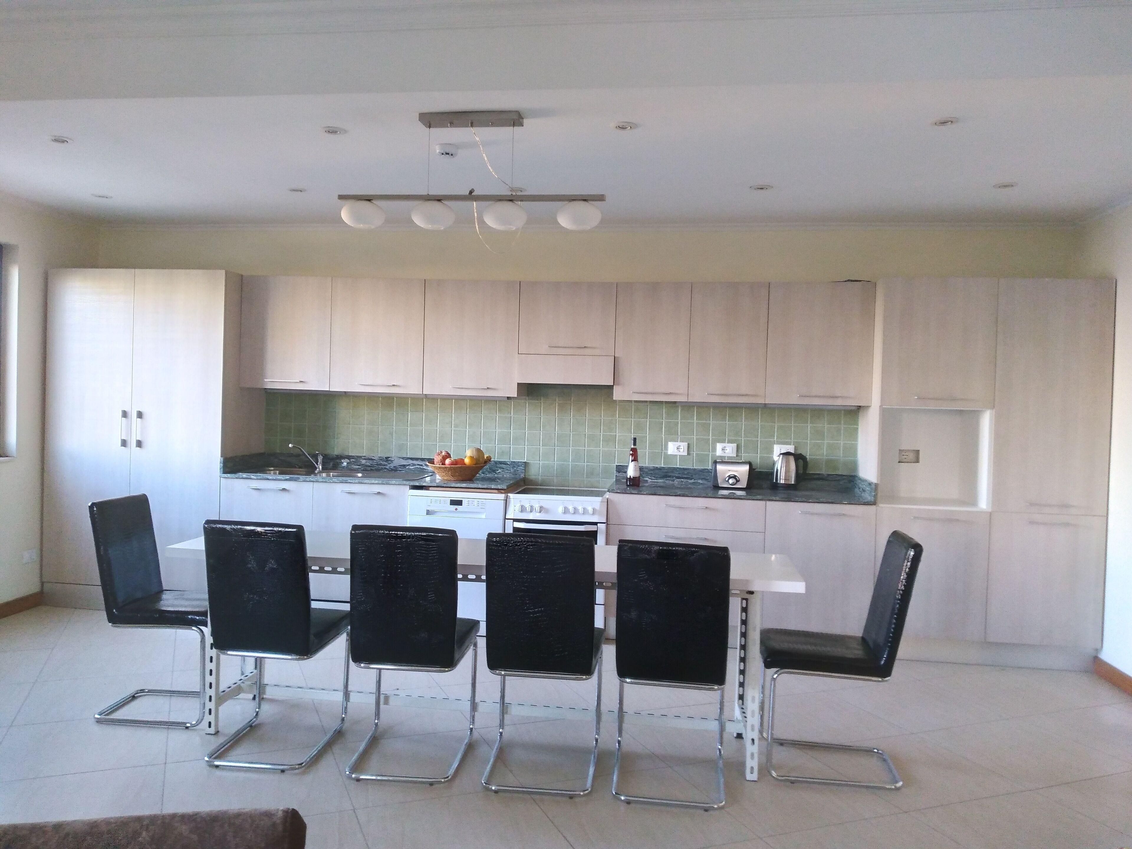 A modern kitchen with light-colored cabinets, a central island, and a dining area with four black chairs.
