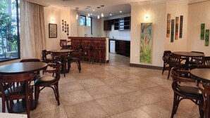 A dining area with multiple wooden tables and chairs, a kitchen in the background, and artwork on the walls. - Kora Hotel Suites (Addis Ababa)