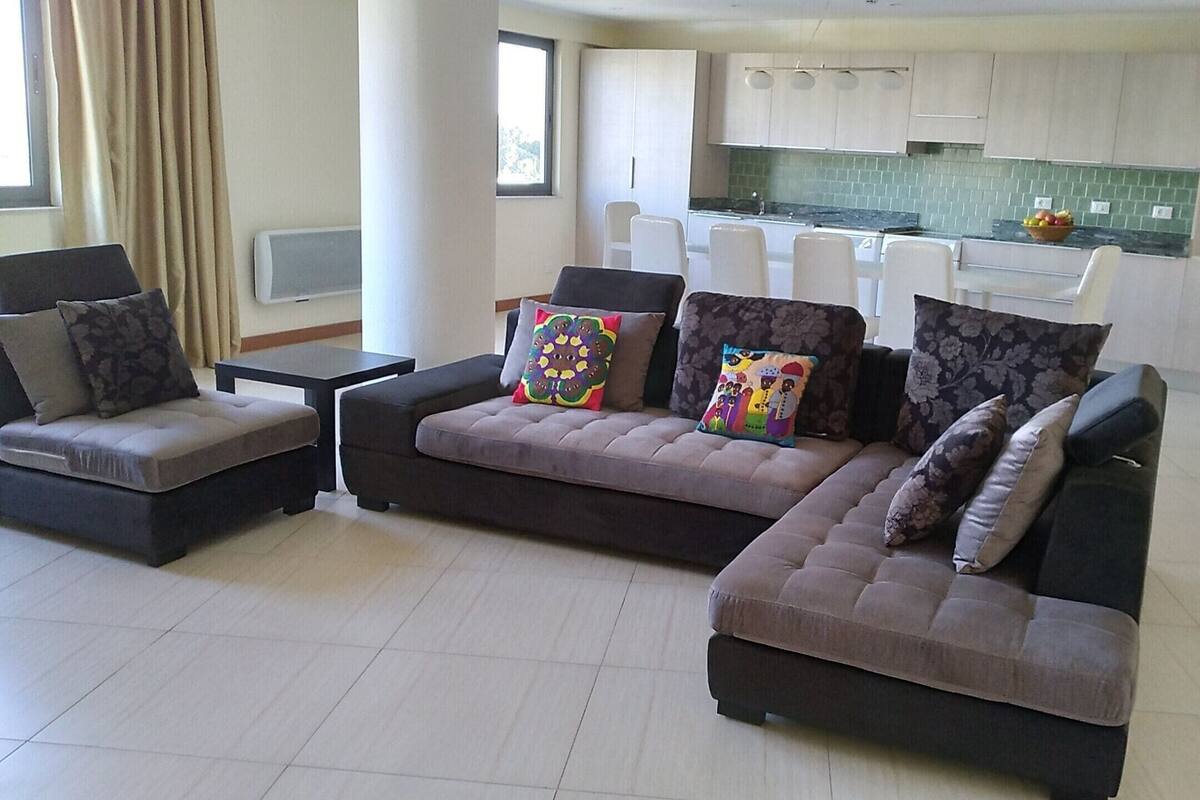 A modern living room with a sectional sofa, a small table, and a kitchen in the background.