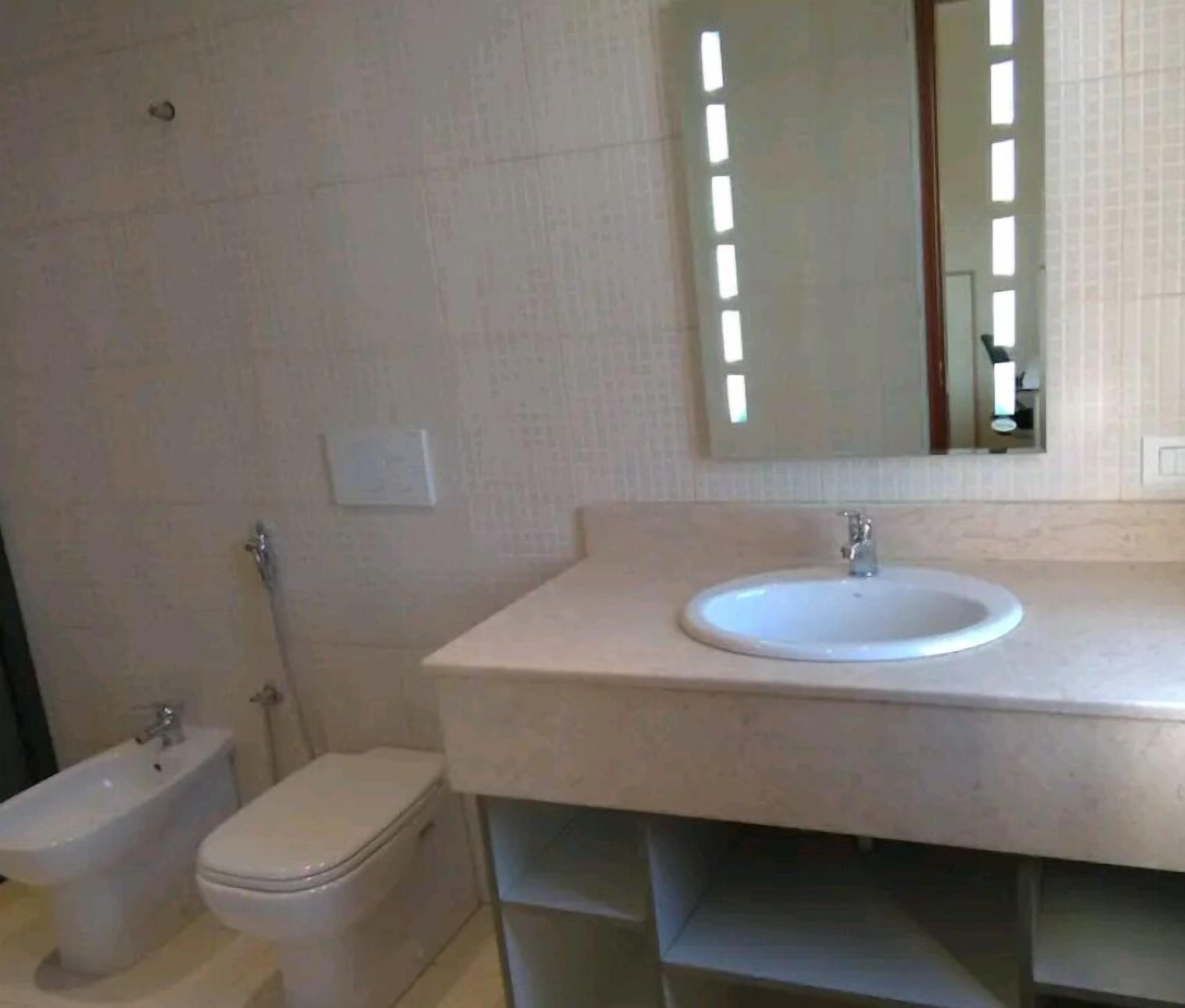 Et badeværelse med toilet, bidet og vask med spejl over.