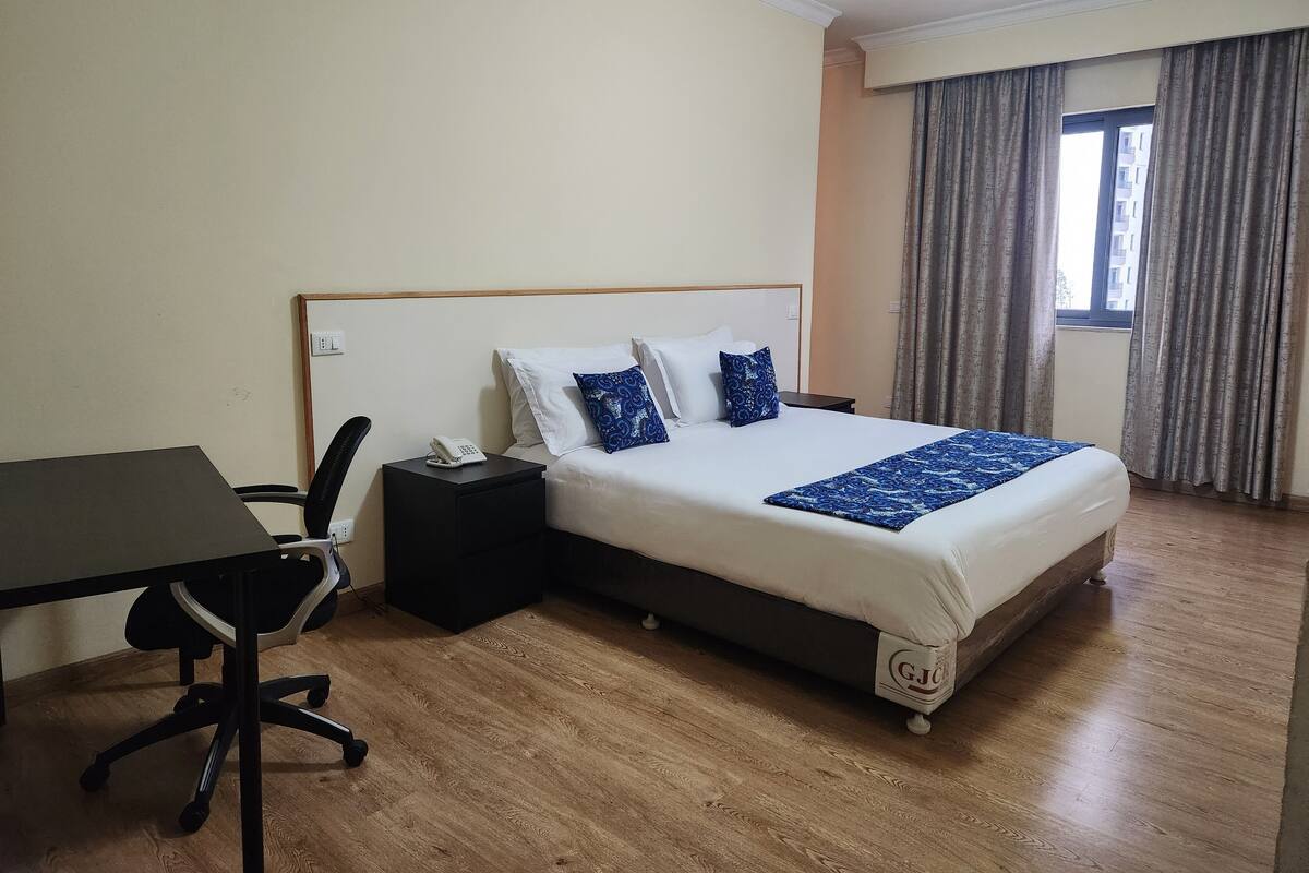 A hotel room with a bed, a desk, a chair, and a telephone.