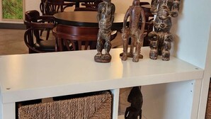 A room with a dining area featuring wooden chairs and a table. There are several wooden sculptures displayed on shelves. - Kora Hotel Suites (Addis Ababa)